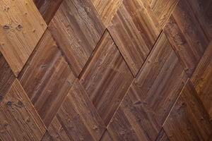 Ein Muster aus holzähnlichen, diamantförmigen Planken in verschiedenen Brauntönen, die eine strukturierte Wandverkleidung darstellen.