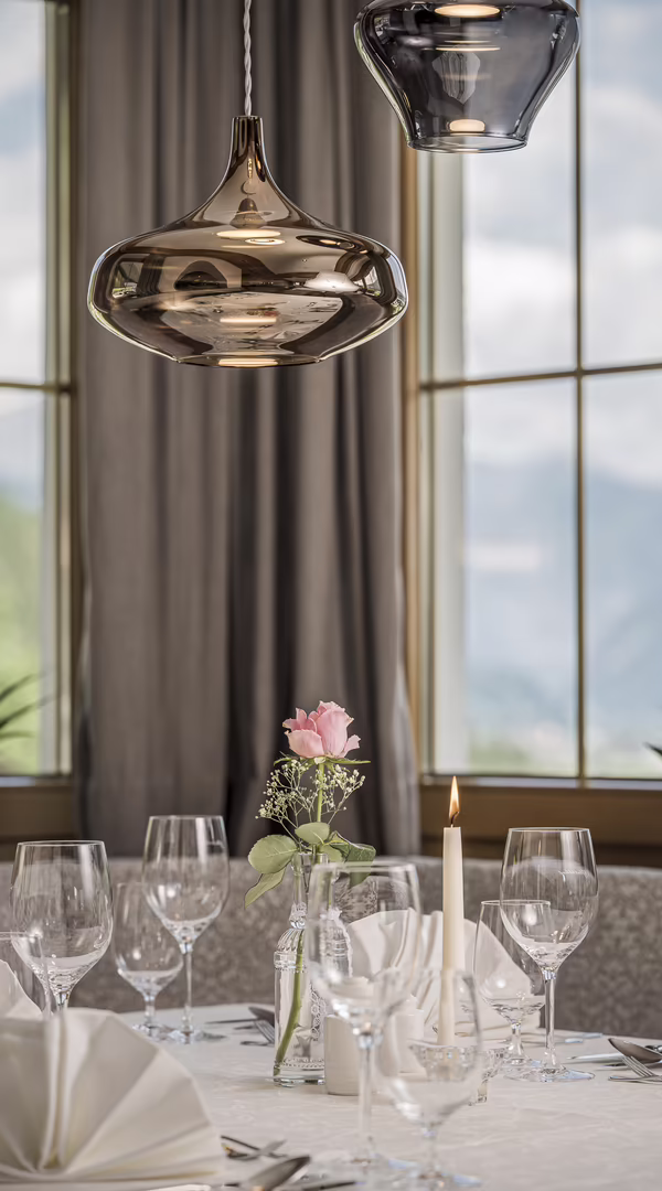Ein elegant gedeckter Tisch mit Gläsern, Servietten und einer Rose in einer Vase, beleuchtet von modernen Hängeleuchten.
