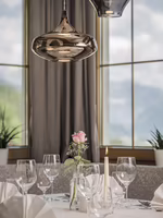 Ein elegant gedeckter Tisch mit Gläsern, Servietten und einer Rose in einer Vase, beleuchtet von modernen Hängeleuchten.