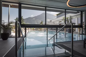 Blick auf den Außenpool des Hotel Platzlhof mit großen Glasfronten und Aussicht auf die Zillertaler Berge.