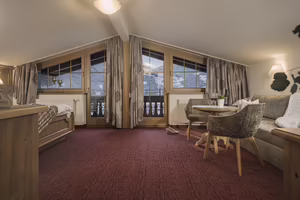 Gemütliches Zimmer mit Panoramafenstern, Teppichboden, einem Bett, einem Sofa und einem Tisch, umgeben von Bergen.