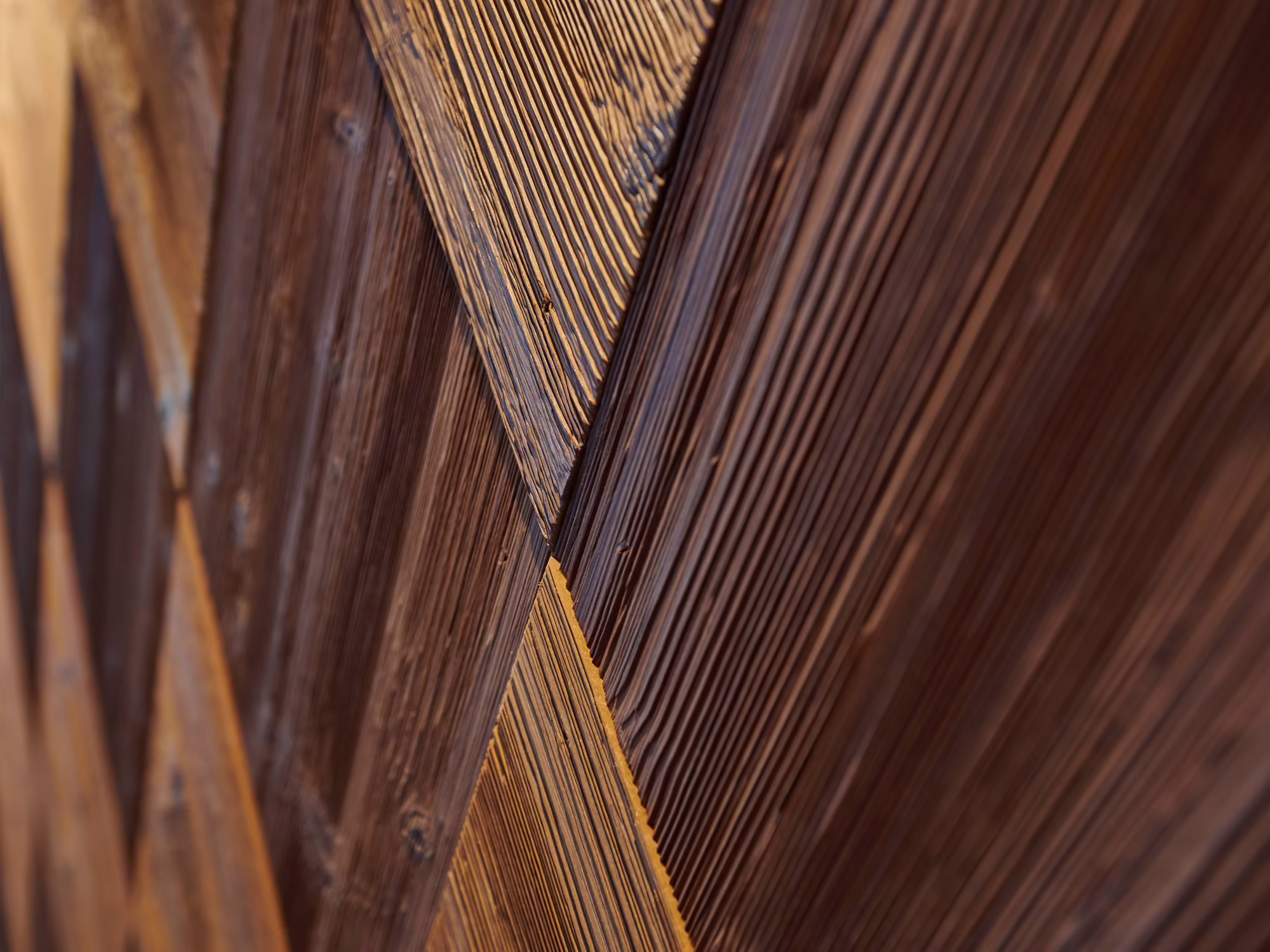 Details in der Rezeption Hotel Platzlhof Eine Holzoberfläche mit diagonal angeordneten, strukturierten Brett- und Fugenmustern in verschiedenen Brauntönen.