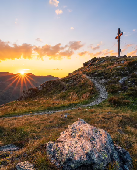 Sommerlicher Sonnenuntergang am Berg mit einem Gipfelkreuz im Foto