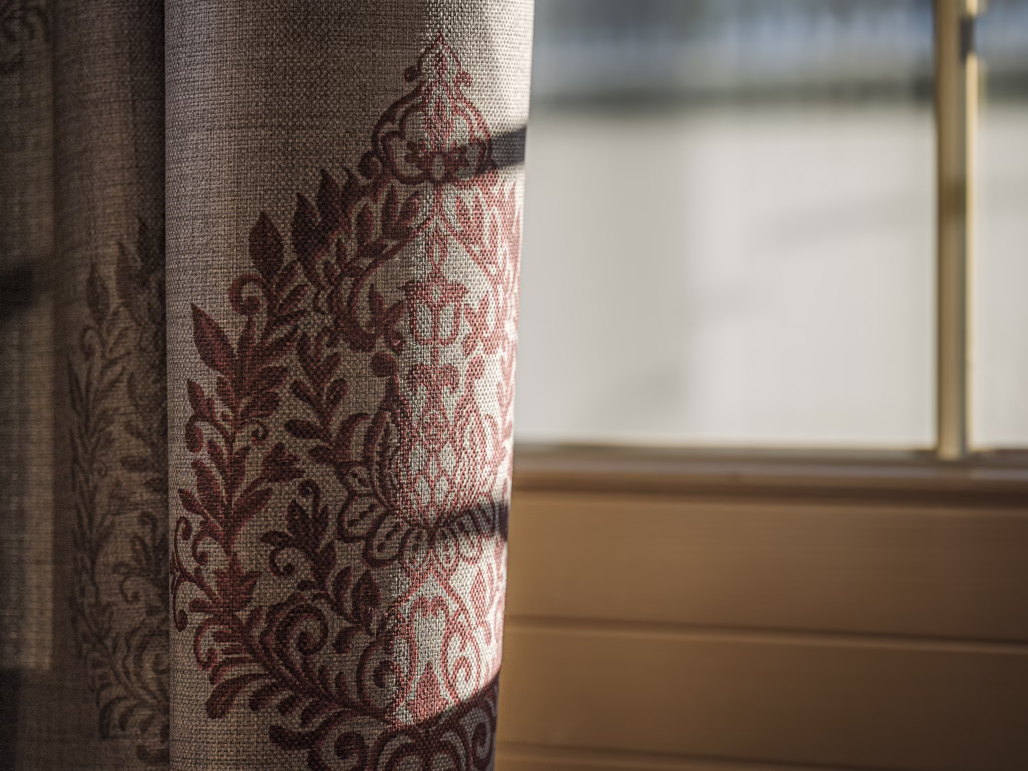 Hochwertige Zimmerausstattung Ein Teil eines mit floralen Mustern verzierten Vorhangs, der sanftes Licht durch ein Fenster einfängt.