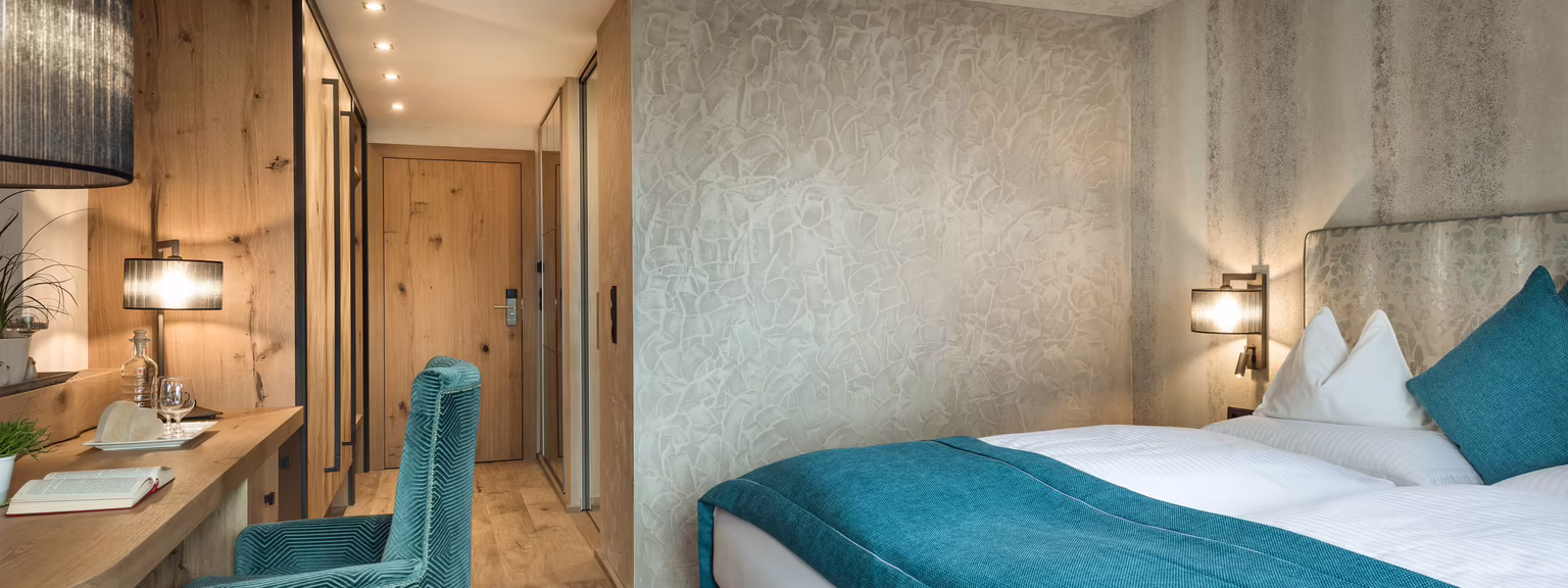 Komfortables Zimmer im Hotel Platzlhof Stilvoll eingerichtetes Zimmer mit Doppelbett, gemütlichem Sessel, Schreibtisch und warmer Beleuchtung.
