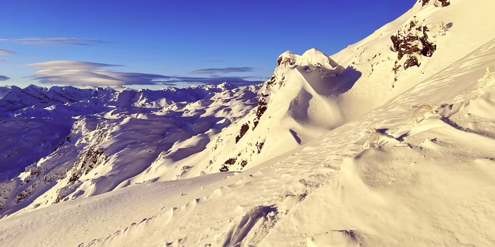 Landschaft in Hochzillertal bei strahlend blauem Himmel Schneebedeckte Berge unter einem klaren blauen Himmel, mit sanften Wellen und Felsen im Vordergrund.