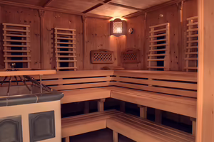 Innenansicht einer Holzsauna mit Bänken und sanfter Beleuchtung. Die Wände sind mit Holz verkleidet und es gibt eine Feuerstelle.