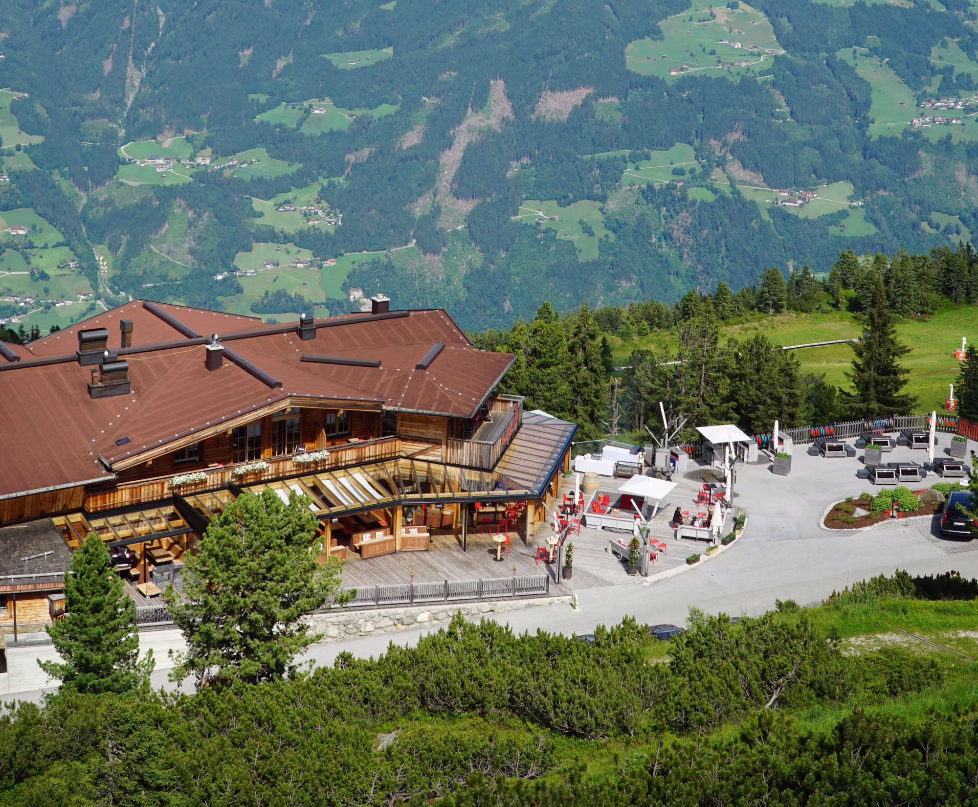 Platzlalm im Sommer mit Bergpanorama Berglandschaft mit einem Holzhaus im Vordergrund und einem weiten Tal im Hintergrund, umgeben von grünen Wiesen und Bergen.