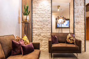 Sitzecke mit braunen Sesseln und Kissen vor einer Natursteinwand in der Lobby des Hotel Platzlhof in Ried im Zillertal