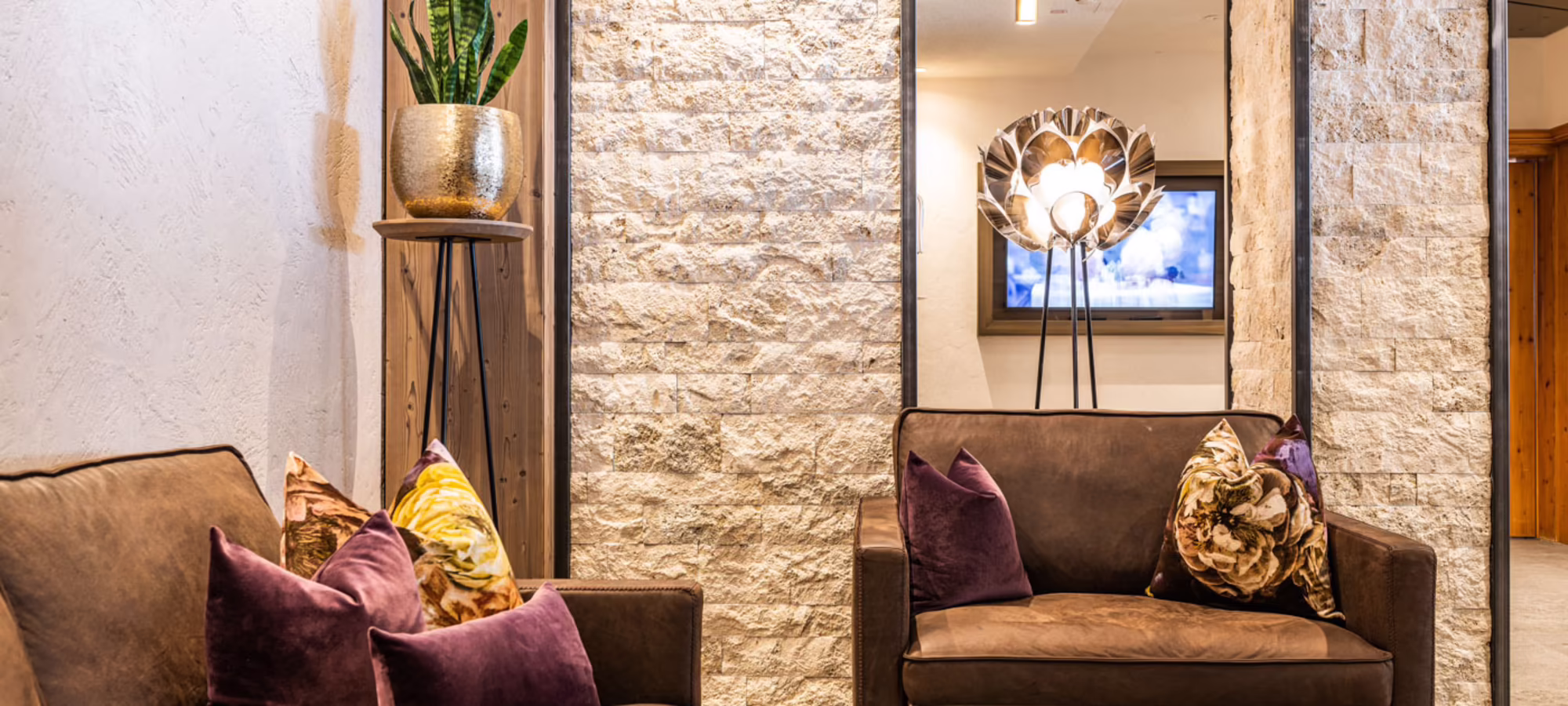 Sitzecke in der Lobby des Hotel Platzlhof Sitzecke mit braunen Sesseln und Kissen vor einer Natursteinwand in der Lobby des Hotel Platzlhof in Ried im Zillertal
