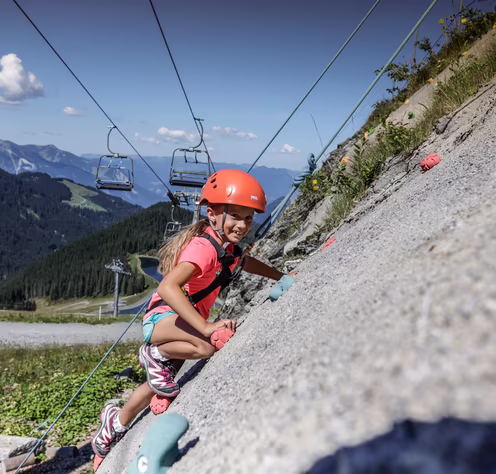Mädchen klettert an einer Felswand mit Helm und Sportausrüstung.
