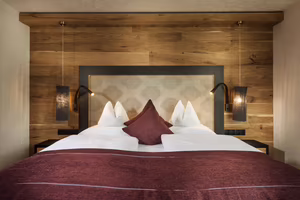 Ein gemütliches Schlafzimmer mit einem Doppelbett, Holzwänden und stilvollen Beleuchtungselementen. Geordnete Bettwäsche in Rot- und Weißtönen.