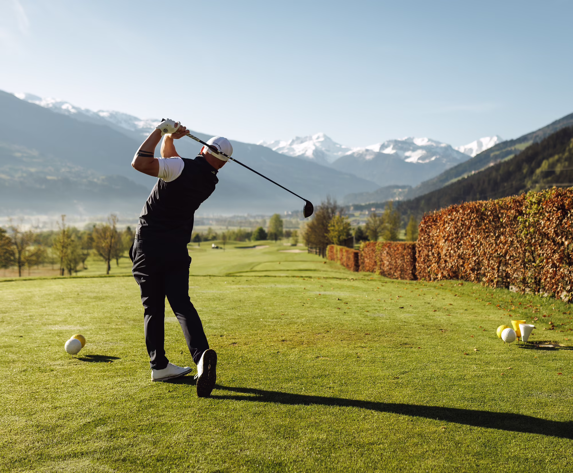 Golfspieler beim Abschlag auf einem Platz mit Berglandschaft im Hintergrund.