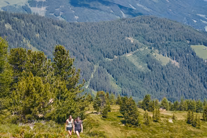 Two women hiking on a green mountain slope with panorama.