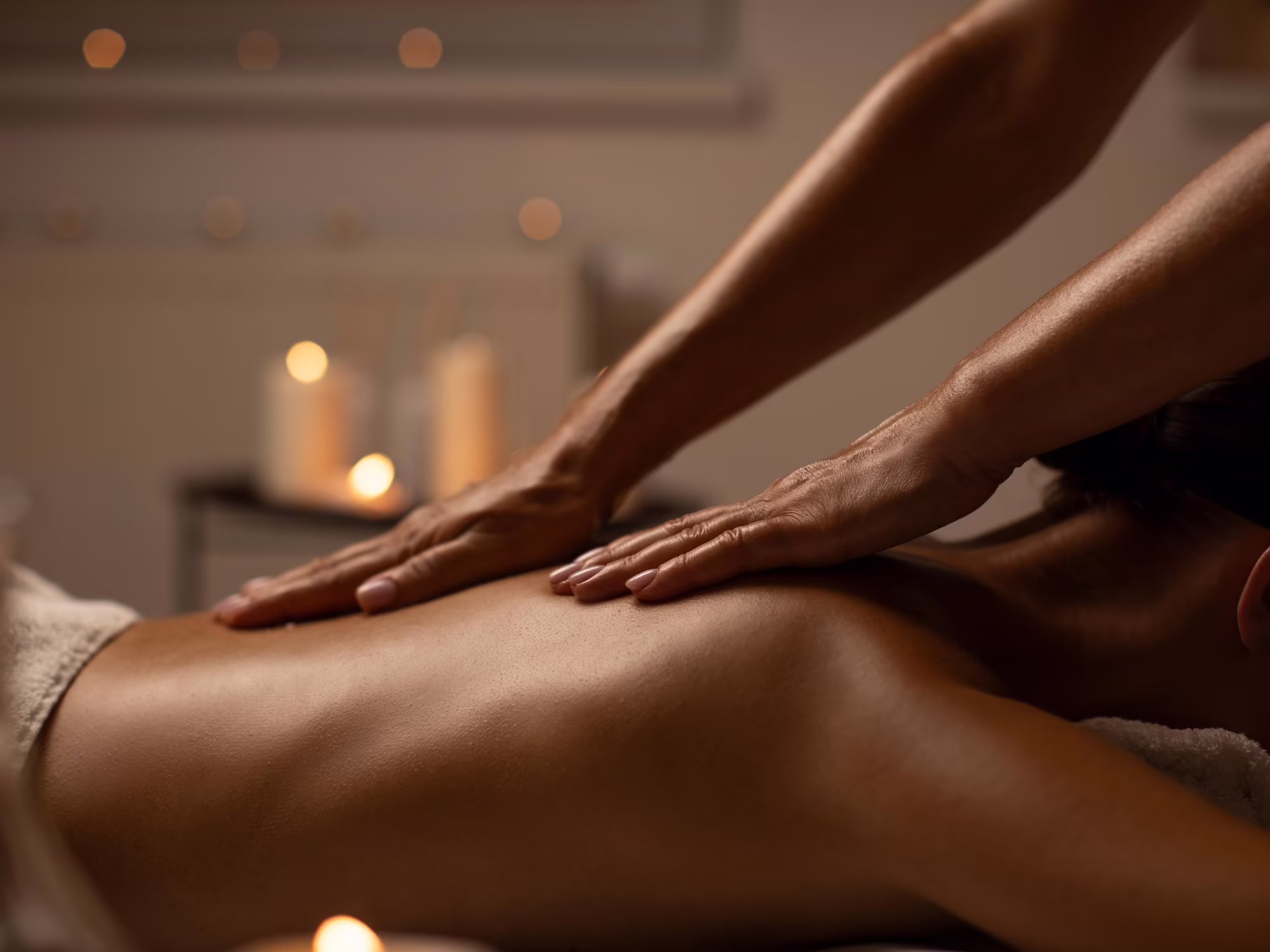 Entspannung pur im Hotel Platzlhof Eine Person erhält eine Massage auf dem Rücken, umgeben von sanftem Licht von Kerzen.