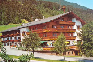 Der Platzlhof im Jahr 1978 Ein traditionelles alpines Hotel mit Holzverkleidung, Balkonen und bunten Sonnenschirmen, umgeben von Bäumen und Bergen im Hintergrund.