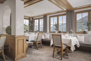 Eine elegante Restaurantinnenansicht mit Tischen, Stühlen, Dekoration und großen Fenstern, die einen Blick auf die Berge bieten.