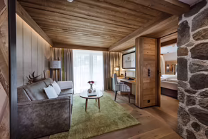 Wohnbereich in Sarah’s Jagasuite mit Sofa, Schreibtisch, viel Holz und Blick in den angrenzenden Schlafbereich.