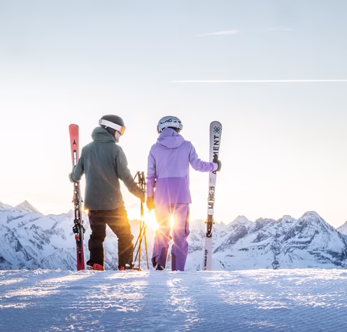 Zwei Skifahrer stehen am Pistenrand und betrachten die Berge.