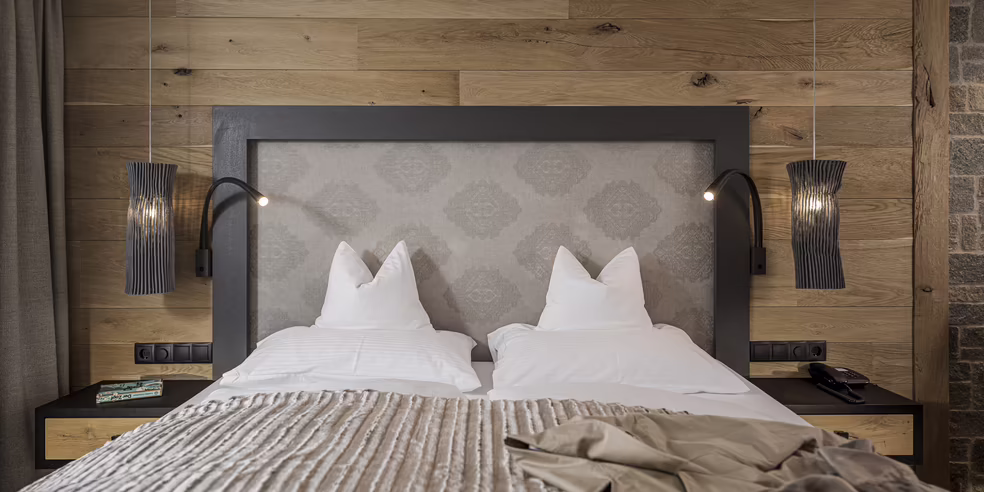 Ein modernes Schlafzimmer mit einem Doppelbett, Holzvertäfelung an der Wand und stilvollen Nachttischlampen.