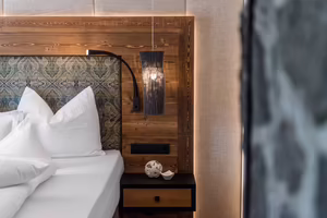 Gemütlicher Schlafbereich in Sarah’s Jagasuite mit Doppelbett, Holzdetails und stilvoller Beleuchtung im Hotel Platzlhof.