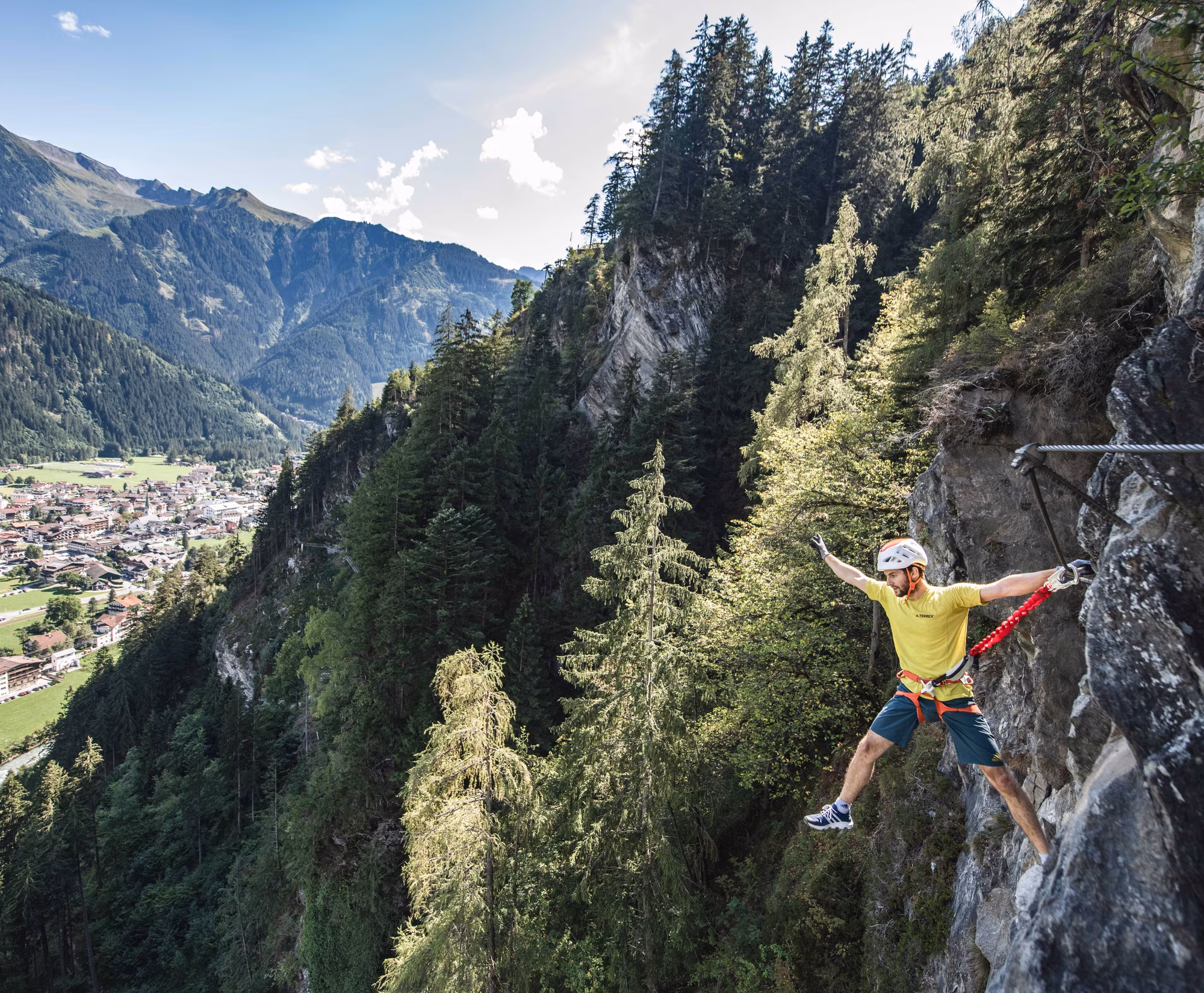 Klettersteig Archiv TVB Mayrhofen © Dominic Ebenbichler Kletterer auf einem Felsen mit Blick auf eine Stadt und Berglandschaft.