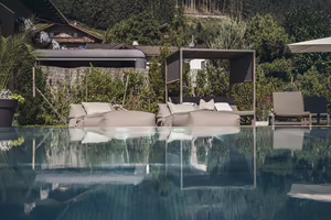 Pool mit Liegen und Sonnenschutz, umgeben von üppigem Grün und modernen Gartenmöbeln. Reflexionen im Wasser sind sichtbar.