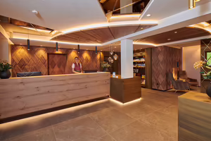 Moderne Hotellobby mit Holzdekoren, Empfangstresen und gemütlichen Sitzgelegenheiten. Eine Mitarbeiterin steht hinter dem Empfang.