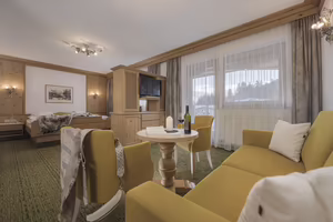 Heller Hotelzimmer mit gelbem Sofa, Tisch, Fernseher und Blick auf die Natur.