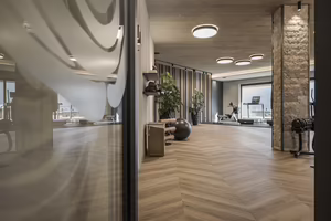 Moderne Fitnessräume mit Holzfußboden, großen Fenstern und verschiedenen Trainingsgeräten, umgeben von Pflanzen und stilvollen Elementen.