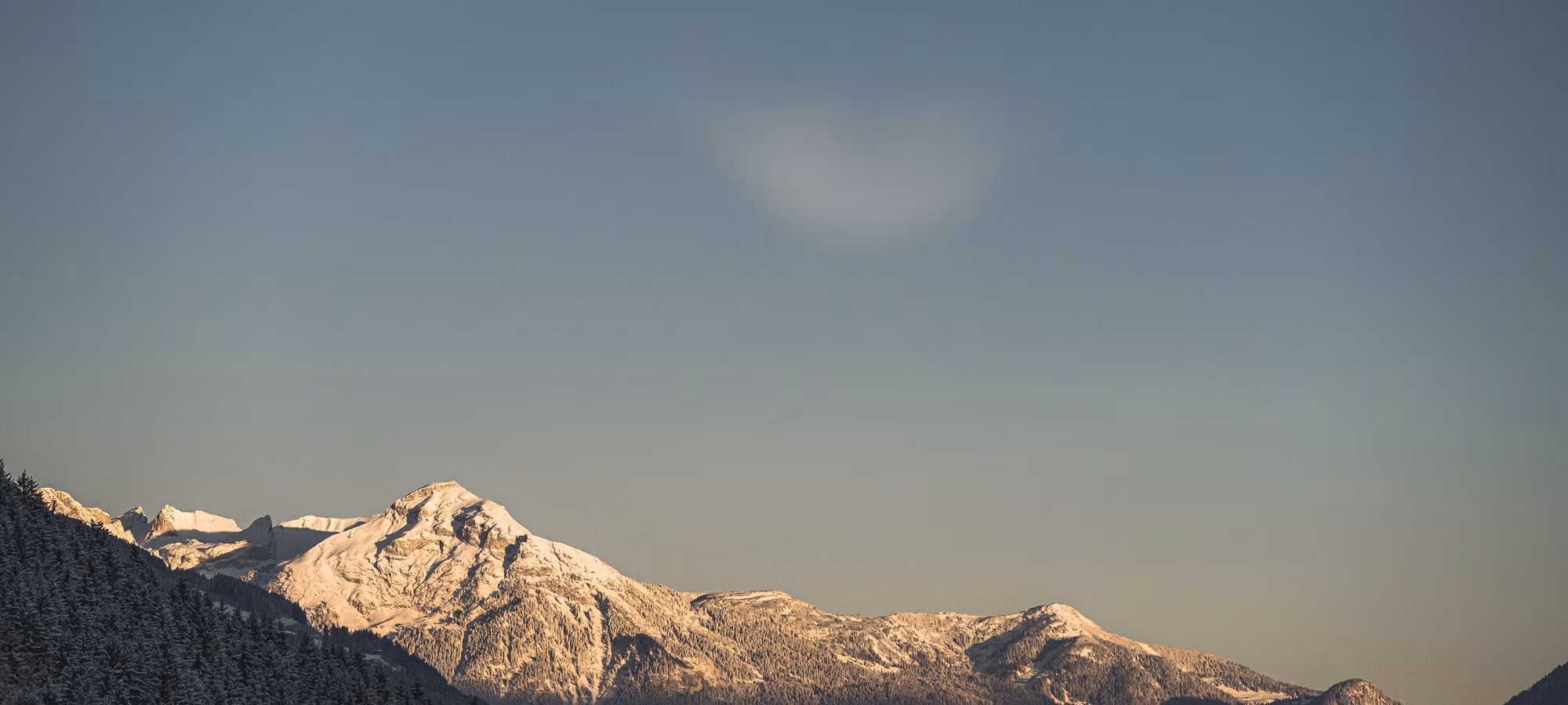 Schneebedeckte Berge unter einem klaren Himmel, mit sanften Schatten und einem subtilen Farbverlauf am Horizont.
