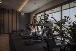 Eine Person trainiert auf einem Ellipsentrainer in einem modernen Fitnessraum mit großen Fenstern und Pflanzen.