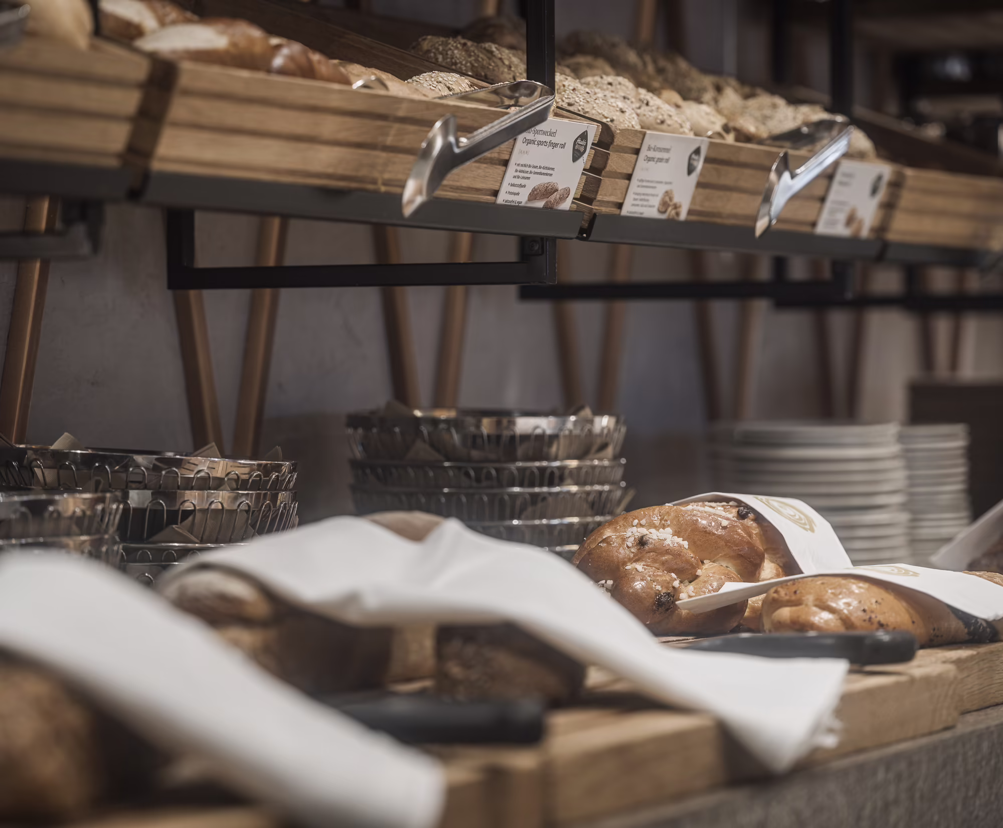 Brotauswahl am Frühstücksbuffet Ein Buffet mit verschiedenen Brotsorten, einige Brote sind in Tücher gewickelt, Holzregale und Schalen im Hintergrund.