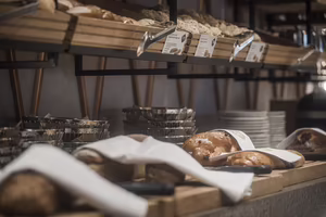 Ein Buffet mit verschiedenen Brotsorten, einige Brote sind in Tücher gewickelt, Holzregale und Schalen im Hintergrund.