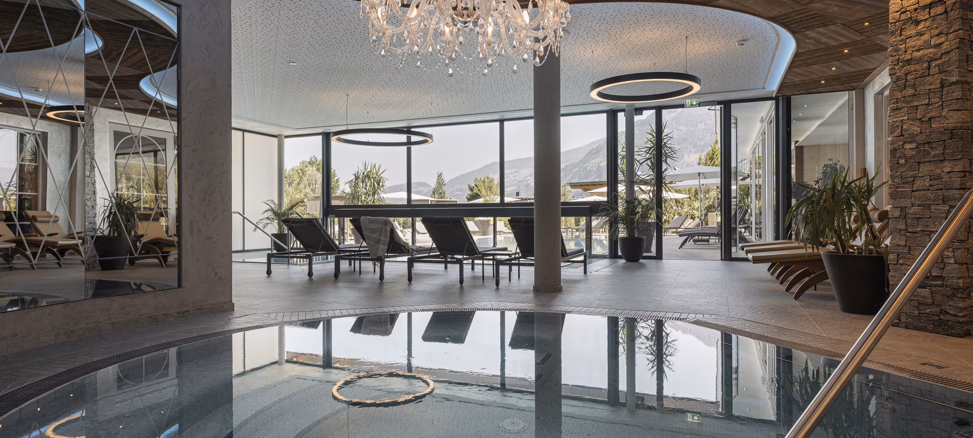 Ein eleganter Wellnessbereich mit einem Whirlpool, Liegen und großen Fenstern, die einen Blick auf die Natur bieten.