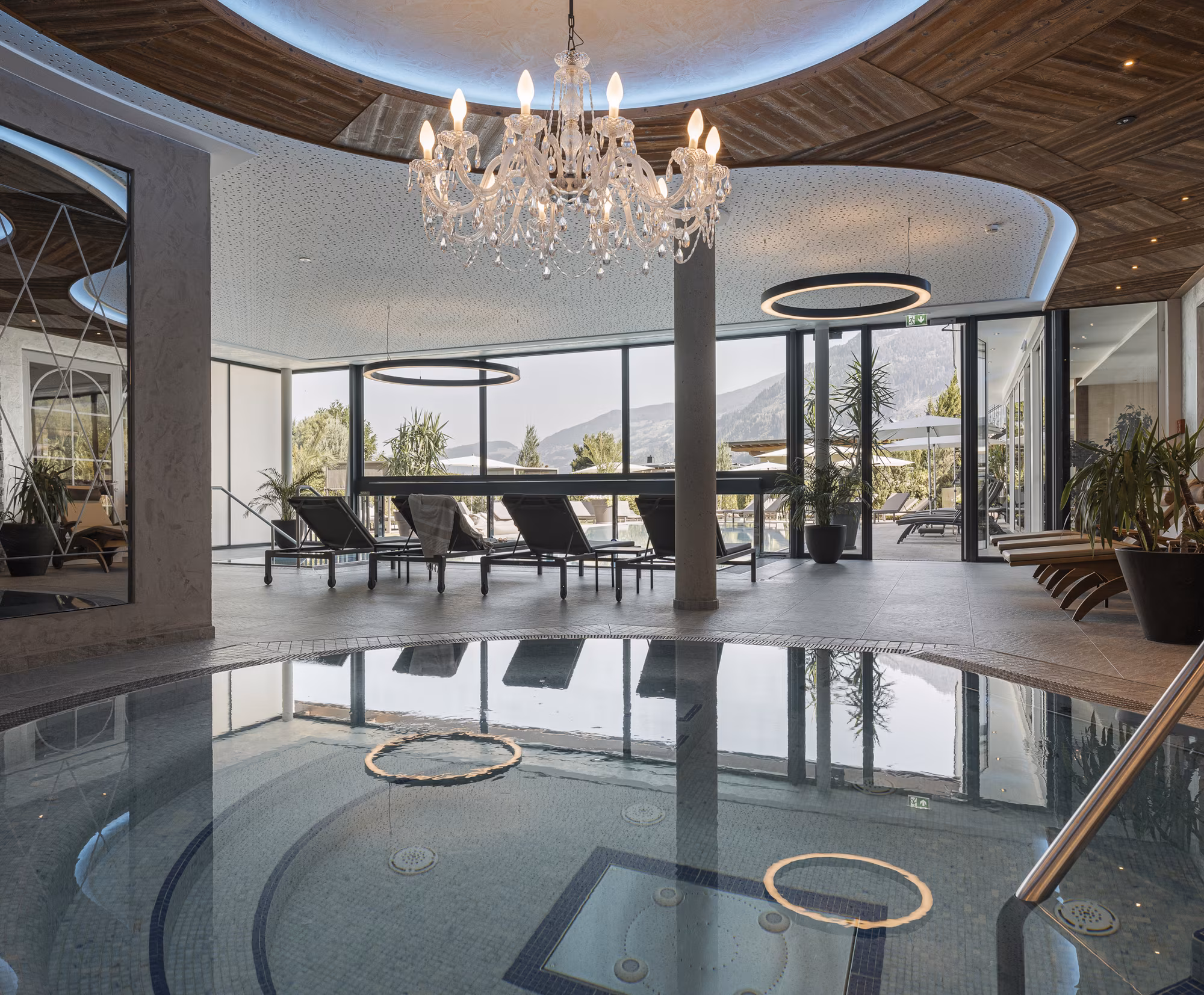Whirlpool im Innenbereich im Hotel Platzlhof Ein eleganter Wellnessbereich mit einem Whirlpool, Liegen und großen Fenstern, die einen Blick auf die Natur bieten.