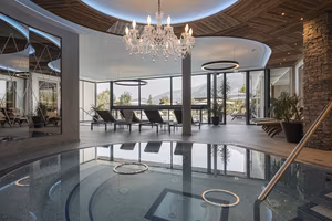 Ein eleganter Wellnessbereich mit einem Whirlpool, Liegen und großen Fenstern, die einen Blick auf die Natur bieten.