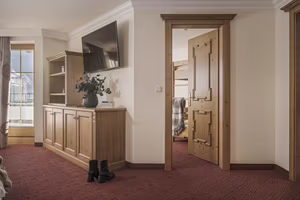 Ein gemütlicher Hotelzimmer-Eingang mit Holzschränken, einem Fernseher an der Wand und einer offenen Tür zum zweiten Schlafzimmer.