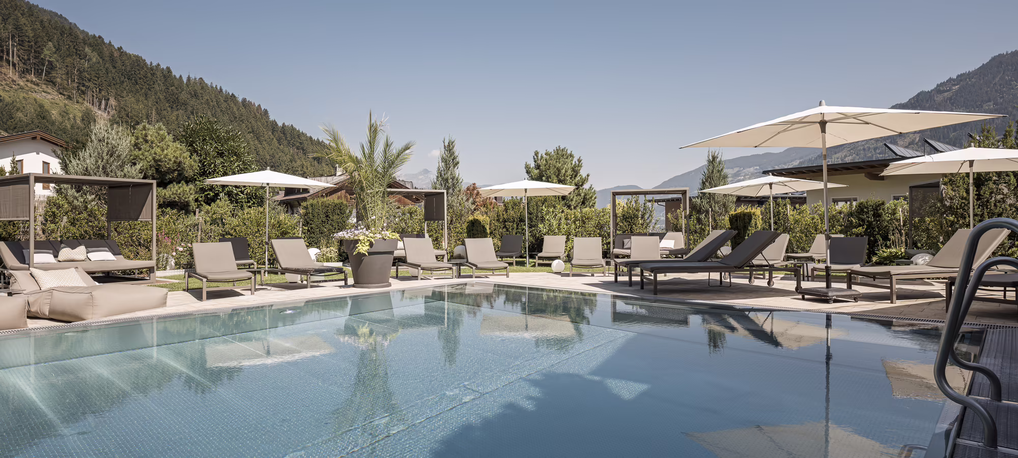 Außenpool mit Sonnenterrasse im Hotel Platzlhof Großzügiger Außenpool des Hotel Platzlhof mit Sonnenliegen, Daybeds und Blick auf die Zillertaler Bergwelt.