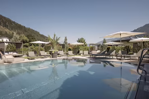 Großzügiger Außenpool des Hotel Platzlhof mit Sonnenliegen, Daybeds und Blick auf die Zillertaler Bergwelt.