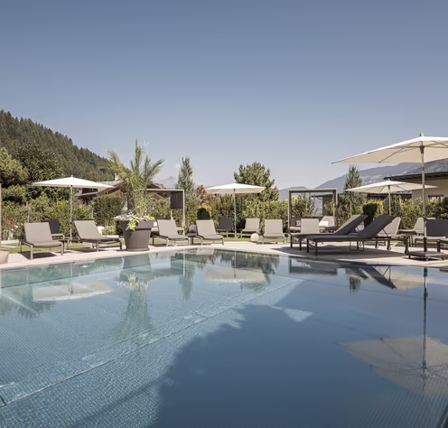 Großzügiger Außenpool des Hotel Platzlhof mit Sonnenliegen, Daybeds und Blick auf die Zillertaler Bergwelt.