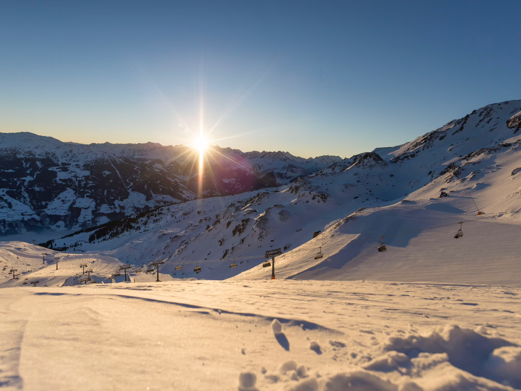 Early Bird Skiing beim Sonnenaufgang in Hochzillertal Sonnenaufgang über schneebedeckten Bergen und eine Umgebung, die von frischem Schnee bedeckt ist.