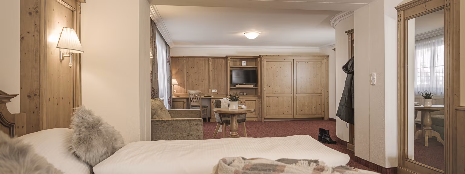 Barrierefreies Schlafzimmer Wohlfühlsuite Rosalie Gemütliches Zimmer mit Doppelbett, Sitzecke und Holzmöbeln.
